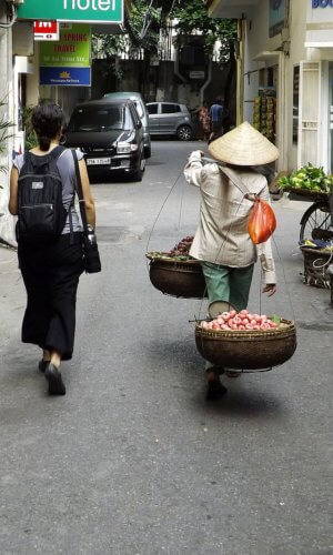 Vendor in old Hanoi, Vietnam walking beside a traveler